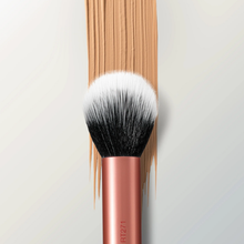 Load image into Gallery viewer, Close-up of the Real Techniques RT271 Skin Tint Base Brush placed over a swipe of beige foundation, highlighting the soft dual-fiber bristles and rose gold handle.