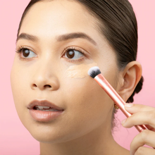 Load image into Gallery viewer, Close-up of cream concealer being blended smoothly under the eye area using the Real Techniques Expert Concealer Brush.