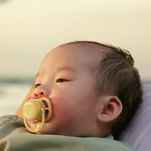 Load image into Gallery viewer, Close-up of a baby using a yellow and red Philips Avent Ultra Air pacifier while resting outdoors.