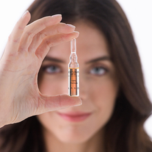 Load image into Gallery viewer, Woman holding a Crescina Transdermic HFSC treatment ampoule in front of her face, showcasing the single-use hair treatment for physiological hair thinning.