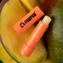 Load image into Gallery viewer, Open Dr. PAWPAW Mango Lip Balm Stick in orange packaging displayed on fresh mango slices, highlighting its tropical mango fragrance.