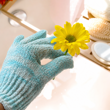 Load image into Gallery viewer, Hand wearing an EcoTools light blue textured exfoliating glove holding a bright yellow daisy flower.