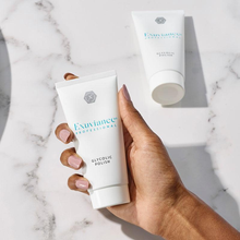 Load image into Gallery viewer, A hand holding a tube of Exuviance Professional Glycolic Polish against a white marble background with a second tube resting in the background.