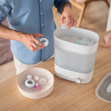 Load image into Gallery viewer, Parent loads Philips Avent sterilizer with bottle parts—perfect for newborn baby essentials.