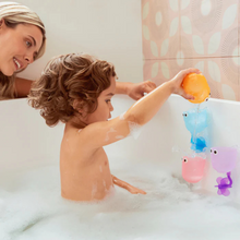 Load image into Gallery viewer, Child pouring water into colorful Munchkin Falls bath toy cups while playing in a bubble-filled bathtub, supervised by an adult