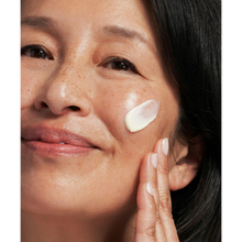 Load image into Gallery viewer, A close-up lifestyle image of a smiling person with freckles applying a streak of NeoStrata Matrix Support cream to their cheek. They are using their fingertips to blend the product into their skin.