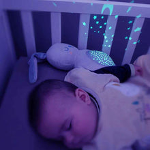 Load image into Gallery viewer, A soft Pabobo Mimi Bunny Plush Projector resting next to a baby in a crib, casting a calming blue star projection on the nursery wall.
