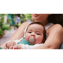 Load image into Gallery viewer, An infant being cradled by an adult while using a rose pink Philips Avent Ultra Soft soother (SCF091/43) in a soft-focus outdoor setting.