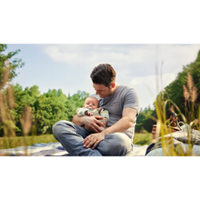 Load image into Gallery viewer, A man holds an infant using a light green Philips Avent Ultra Air Night Time sloth soother while sitting on a blanket in a sunny meadow.