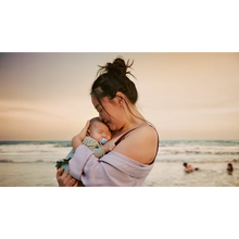 Load image into Gallery viewer, A woman holding a sleeping baby who is using a light blue Philips Avent Ultra Air soother while standing on a beach at sunset.