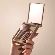 Load image into Gallery viewer, Hand holding the Real Techniques On-The-Glow Mini Makeup Brush Set with mirrored compact open to display five portable mini brushes.