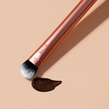 Load image into Gallery viewer, A Real Techniques 210 makeup brush angled next to a smooth swatch of liquid cream product on a neutral background.