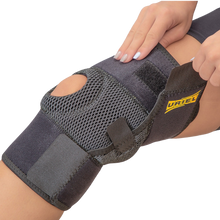 Load image into Gallery viewer, Close-up of the Uriel Knee Support being secured around the knee, highlighting the breathable mesh panel, open patella design and adjustable fastening.