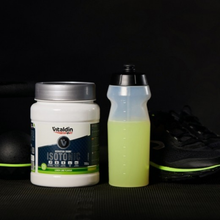 Load image into Gallery viewer, A jar of Vitaldin Sport lime isotonic powder next to a prepared green hydration drink and fresh lime slices on a gym floor.