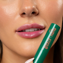 Load image into Gallery viewer, Close-up of a person holding the green WICKED x Dr. PAWPAW Enchanting Lip Balm beside their pink-tinted lips, showcasing the colour-changing lip balm.