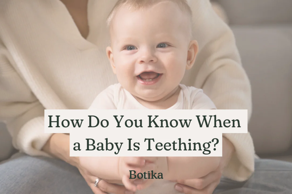 Smiling teething baby in parent’s lap with blog title “How Do You Know When a Baby Is Teething” overlayed.