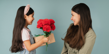 A little girls presents flowers and a gift to a smiling mother, creating a moment of joy and connection between them.