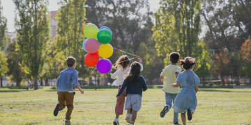 Children joyfully running in a park, each holding vibrant balloons of various colours.