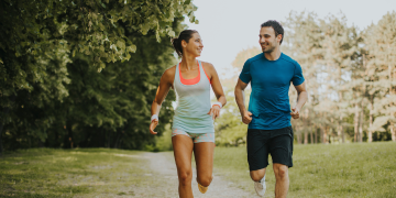 Two people jogging side by side on a sunlit path through a park.