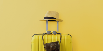 Yellow suitcase adorned with a hat and sunglasses, set against a vibrant yellow background.