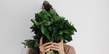 Woman holds a bunch of leafy greens in front of her face.
