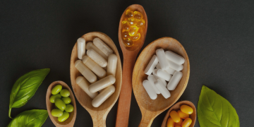 A collection of wooden spoons filled with various vitamins and supplements arranged on a neutral background.