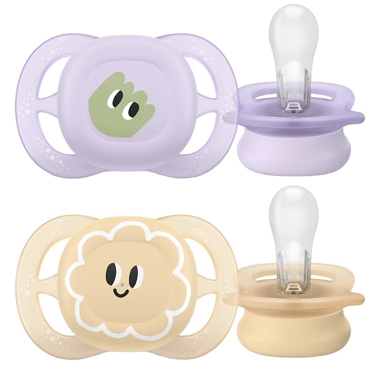 Two Philips Avent pacifiers with holders, one with a green character design and the other with a pink floral design, both in beige color.