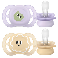 Two Philips Avent pacifiers with holders, one with a green character design and the other with a pink floral design, both in beige color.