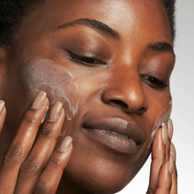 Load image into Gallery viewer, Woman applying cream to her face with a neutral background
