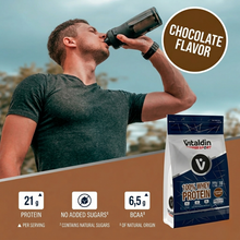 Load image into Gallery viewer, A promotional square-format graphic for Vitaldin Sport 100% Whey Protein. The top half shows a man in a gray t-shirt drinking from a protein shaker outdoors. A large brown circle on the right reads "CHOCOLATE FLAVOR." The bottom half features a product bag and three icons: 21g Protein per serving, No Added Sugars (contains natural sugars), and 6.5g BCAA of natural origin.
