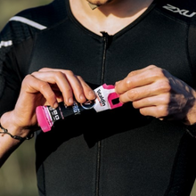Load image into Gallery viewer, A close-up of an athlete in a black compression shirt holding and opening a Vitaldin Sport Energy Gel pouch in Strawberry and Banana flavor. The athlete's hands are positioned to tear the top of the pink and black packet.
