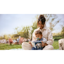 Load image into Gallery viewer, Happy baby wearing Philips Avent Ultra Air pacifier while sitting with mother and reading a soft book in a sunny park.
