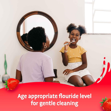 Load image into Gallery viewer, A young girl brushing her teeth in a bathroom mirror with her mother, emphasizing the age-appropriate fluoride level for gentle cleaning.
