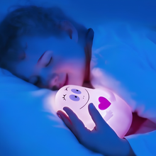 Load image into Gallery viewer, Young child sleeping peacefully in bed while holding a glowing, cute character night light with a smiling face and heart.
