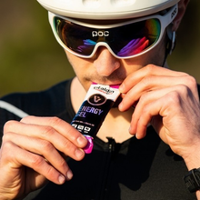 Load image into Gallery viewer, A close-up of a cyclist wearing a white helmet and performance sunglasses, consuming a Vitaldin Sport Strawberry and Banana Energy Gel while on a ride.

