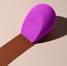 Load image into Gallery viewer, EcoTools BioBlender purple makeup sponge resting on a dark liquid foundation swatch on a beige surface.
