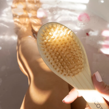 Load image into Gallery viewer, Close-up of a hand holding the EcoTools foot brush bristle head over a relaxing bathtub.
