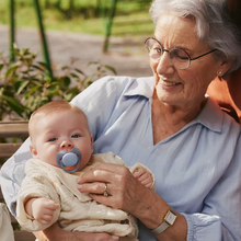 Load image into Gallery viewer, An older woman smiling while holding a baby, who is comfortably using a beige Philips Avent pacifier.
