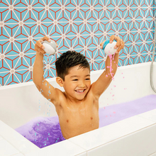 Load image into Gallery viewer, Smiling child in the bath plays with Munchkin dispensers and purple-coloured bath water.
