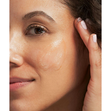 Load image into Gallery viewer, A close-up lifestyle image of a person applying a clear, glistening layer of NeoStrata Exfoliating Mask to their cheek. The person has their fingers near their temple as they blend the product into the skin.
