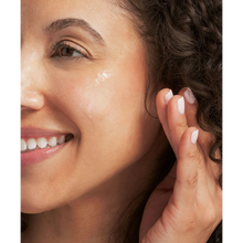 Load image into Gallery viewer, A close-up lifestyle image of a person with curly hair smiling while applying clear NeoStrata Clarify Gel Plus to their cheek. The person’s skin appears glowing and hydrated, and they have a clean, white manicure.
