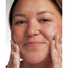 Load image into Gallery viewer, A close-up lifestyle image of a person with fair skin and a neutral manicure smiling while massaging NeoStrata Mandelic Clarifying Cleanser onto their face, showing the white lather on the forehead and cheeks.
