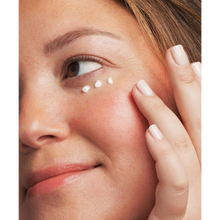 Load image into Gallery viewer, A close-up lifestyle image of a person smiling while applying NeoStrata Restore PHA Eye Cream. Three small dots of white cream are placed under the eye, and the person is using their ring finger to gently pat the product into the skin.
