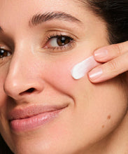 Load image into Gallery viewer, A close-up lifestyle image of a person with fair skin applying a streak of white face cream to their cheek with their fingertips.
