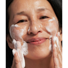 Load image into Gallery viewer, A close-up lifestyle image of a person with freckles smiling while massaging the white NeoStrata Exfoliating Wash foam onto their face.
