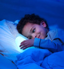 Load image into Gallery viewer, A young child smiling while cuddling the Pabobo Lumilove Glowing Companion nightlight, which provides a reassuring soft light for sleep.
