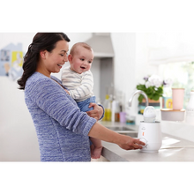 Load image into Gallery viewer, Parent using the Philips Avent Fast Bottle Warmer while holding a baby
