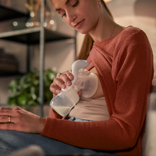 Load image into Gallery viewer, A mother comfortably sitting and using a Philips Avent manual breast pump to express milk into a bottle.
