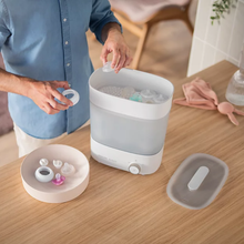 Load image into Gallery viewer, Parent placing baby bottle parts and feeding accessories into the Philips Avent Premium Steriliser &amp; Dryer

