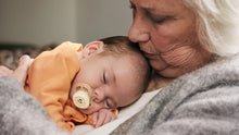 Load image into Gallery viewer, A sleeping newborn baby wearing an orange shirt and using a beige Philips Avent Starter soother while being held by an elderly woman.
